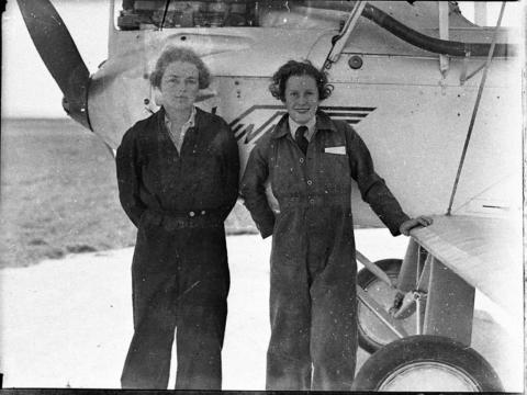 Peggy Kelman (left) with Nancy-Bird Walton (right) standing in front of a plane in pilot gears 