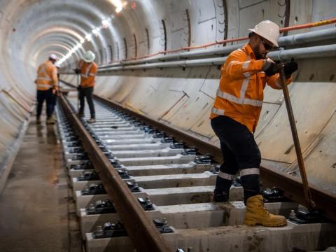 Three construction workers in high viz and hard hats are working on the installation of the track in the tunnel under Sydney Harbour.