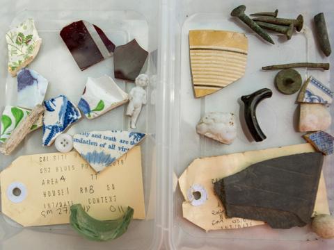 Old artefacts that were found at Blues Point construction site are featured inside a clear plastic container. Some include broken china, glass, a button, and an old label.
