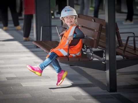 A child sitting on a bench wearing PPE vest, hardhat and glasses at Sydney Metro's Tallawong Station as part of the community day event.