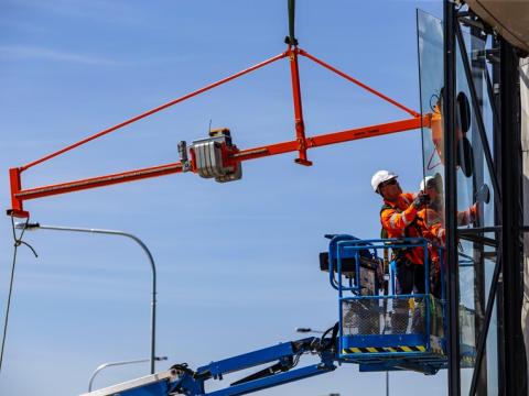 A close up shot of two construction workers installing glass windows from a cherry picker at Sydney Metro's Kellyville Station. 