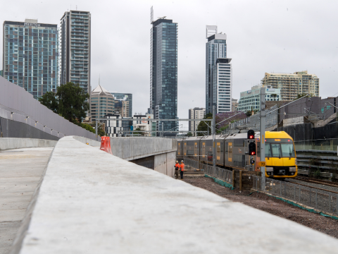 A Sydney train passing by the Chatswood Dive site. There are high rise buildings in the background.
