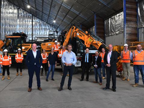 Construction workers and Sydney Metro executives pose for a photo at a construction site with heavy machinery in the background.