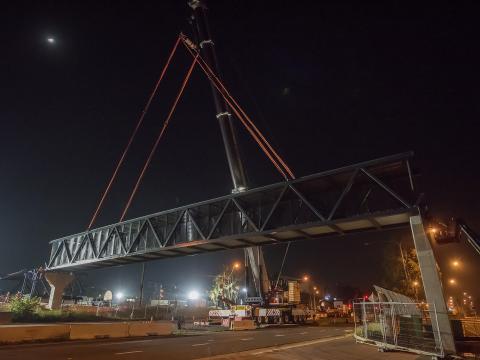 Construction on the Bella Vista pedestrian bridge at night time. The bridge crosses over a large road with many trucks and machinery on site.