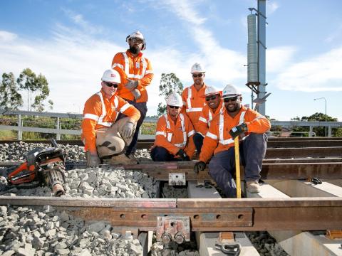 A group of six construction workers sitting on the train tracks as the final track is laid on the Sydney Metro Northwest line in April 2018.