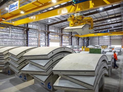 An on the ground shot showing rows on precast concrete segments lined up for production with a machine liftin one of the segments into place at Marrickville precast facility. 