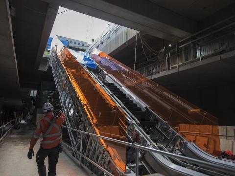 An on the ground view showing the construction of the escalators at Sydney Metro's Norwest Station as a construction worker walks past carrying material them. 