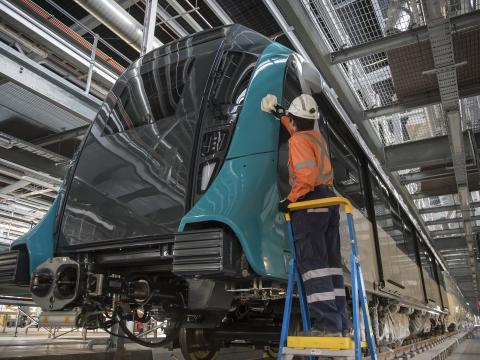 A close up shot showing a Sydney Metro employee in full PPE up standing on a foot ladder cleaning the new Sydney Metro train.