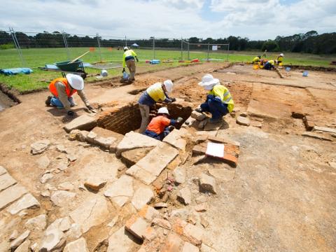 Five construction workers in the foreground and three in the background inspecting the ground for archaeological artefacts during the excavation at Sydney Metro's White Hart Inn site. 