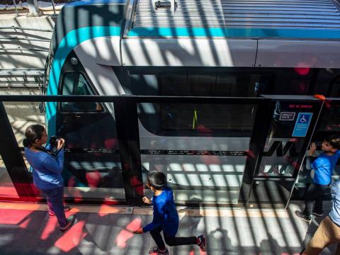 An Arial view of a Sydney Metro train stopped at the platform with commuters standing outside the screen doors.