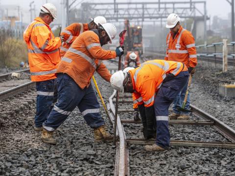 A group of construction workers in orange high-vis are placing the new metro tracks into place at Bankstown Station.