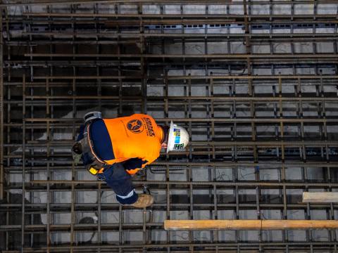 A construction worker bends over using a hand drill on the metal track supports inside Sydney Metro's Victoria Cross station.