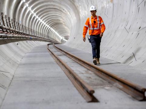 Man in high-vis walking through tunnel with tracks recently layed down.