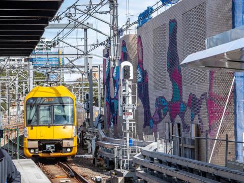 Colourful aboriginal artwork covers the brick ventilation buildings along the tracks at Central Station while a yellow train is approaching the platform.