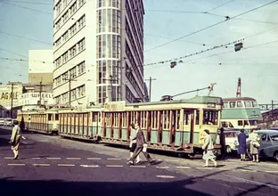 An image from 1957 of the corner of Elizabeth and Chalmers Street, Surry Hills showing commuters crossing the road with a tram on the tracks, cars parked and a bus in the background (Image is from City of Sydney Archives: 044664)