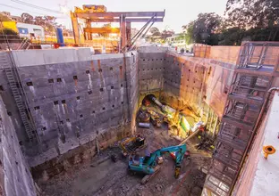 A bird's eye view from the ground looking down into the construction site showing four excavators digging and machines entering the tunnel at Sydney Metro's Epping Services facility. 