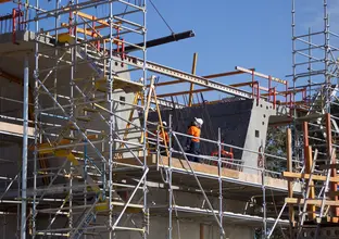 Two construction workers on the scaffolding surrounding the segment of concrete construction on Sydney Metro's skytrain. 
