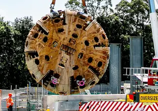 TBM4 Maria cutterhead is being lifted from Epping construction site while construction workers look on.