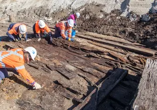 Archaeologists in high vis and hard hats are on their hands and knees while working in the excavation area at the future site of Barangaroo Metro Station where an old boat was found.