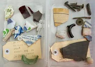 Old artefacts that were found at Blues Point construction site are featured inside a clear plastic container. Some include broken china, glass, a button, and an old label.