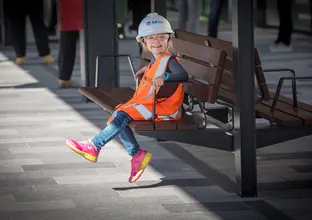 A child sitting on a bench wearing PPE vest, hardhat and glasses at Sydney Metro's Tallawong Station as part of the community day event.