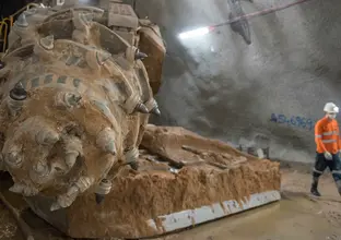 A construction worker walks beside a large muddy Roadheader while inside the tunnels underneath Bligh Street.