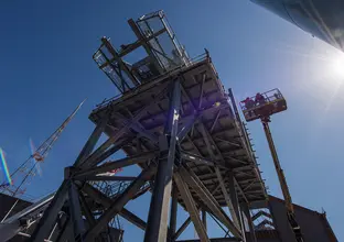 An on the ground view looking up under the conveyer belt as two construction workers are inspecting above from a cherry picker at Sydney Metro's Chatswood Drive.