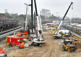 An arial view looking across at the construction site of the Sydney Metro station box at Central Station with many heavy machinery on the ground between the platforms. 