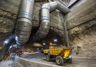 An on the ground view looking across to the tunnel at Sydney Metro's Pitt Street North construction site with two large pipes running through and out of the tunnel and a Roadheader about to drive into the tunnel. 