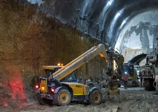 An on the ground view inside the cavern showing two excavators and a larger machine in the background as a construction worker is walking through the machines with a head torch on at Sydney Metro's Martin Place Station.