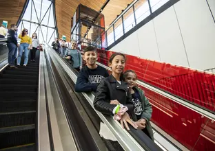 Three children pose while riding down the escalator at Castle Hill Station. A number of people are also on the escalator behind them.