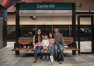 A mother and father pose with their two children sitting on a bench at Sydney Metro Castle Hill Station platform.