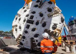 An on the ground view of a construction worker looking up at the cutterhead of a Tunnel Boring Machine (TBM) at Marrickville.
