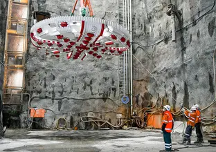 An on the ground view of three construction workers moving into place the overhead Cutterhead Lift of Tunnel Boring Machine (TBM) Mum Shirl at Sydney Metro's at Barangaroo site.