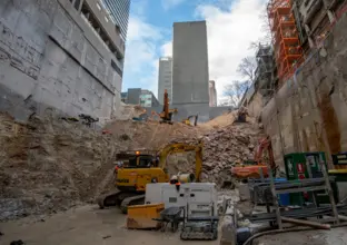 Heavy machinery inside the pit of Victoria Cross South construction site. A few buildings can be seen on ground level above the pit.