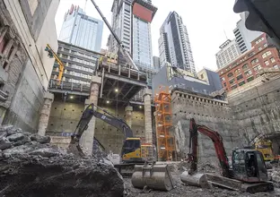 An on ground view looking up at heavy vehicle machinery working inside the Pitt Street South construction site. Tall buildings can be seen in the background.