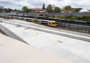 A Sydney train passing by the Chatswood Dive site. There are houses in the background.