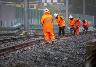 5 construction workers in high viz, using a tool to realign the train track.