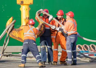 An on the ground view of four construction workers fixing a rope loop onto a crane hook to lift the Tunnel Boring Machine cutterhead at one of Sydney Metro's construction sites.