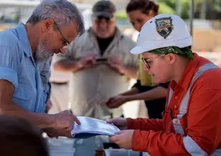 Sydney Metro employees showing community members the archaeological artefacts found at Waterloo Station as they both point to a booklet labelling the displayed artefacts on the table below them. 