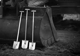 A black and white image of three shovels sitting against a heavy machinery vehicle as construction gets underway on the Sydney Metro West project.