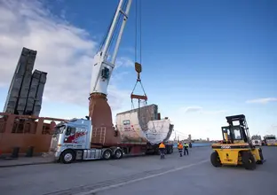 An on the ground view showing Tunnel Boring Machine (TBM) 1 Elizabeth being craned onto a large truck as it arrives in Australia.