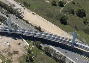 A bird's eye view of Sydney Metro's Windsor Road bridge being constructed, there are cars traveling on the road below.