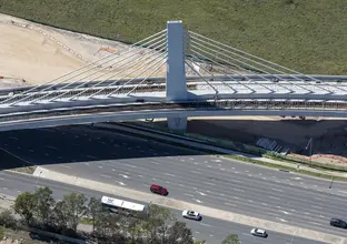 A bird's eye view of Sydney Metro's Windsor Road bridge being constructed, there are cars traveling on the road below.