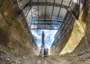 An on the ground view looking up inside the construction site with an excavator machine in the centre of the picture at Sydney Metro's Hills Showground Station box. 