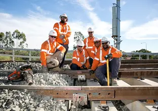 A group of six construction workers sitting on the train tracks as the final track is laid on the Sydney Metro Northwest line in April 2018.