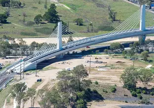 A bird's eye view of the completed bridge section showing cable stayed design with a train running along the tracks.