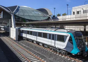 An above the ground view looking down at the first Sydney Metro train arriving at the platform of the city's first metro station showing the station in the background. 