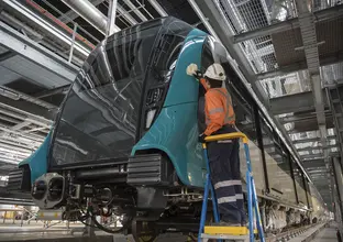 A close up shot showing a Sydney Metro employee in full PPE up standing on a foot ladder cleaning the new Sydney Metro train.