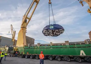 A massive crane lifts part of a TBM off a boat at Newcastle Port while construction workers look on.